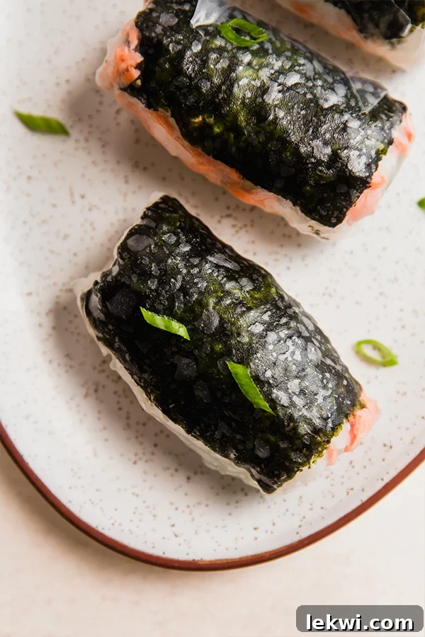 Two salmon rice paper "sushi" rolls on a plate, garnished with green onion.