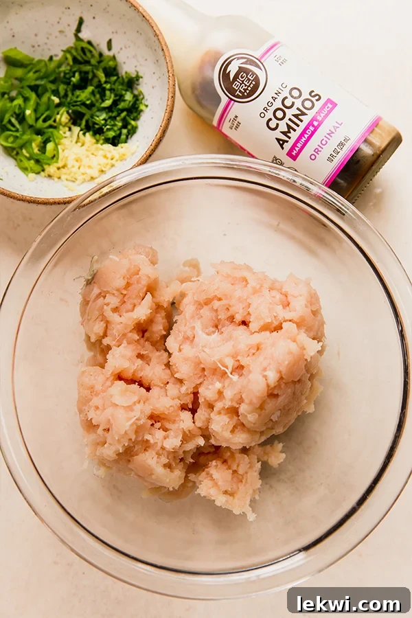 A close-up shot of the raw ingredients for the dumpling filling, including ground chicken, chopped bok choy, green onions, and grated ginger and garlic.