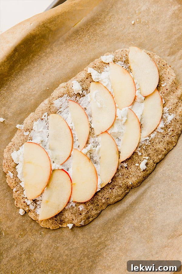 A partially baked apple balsamic flatbread with cheese and thinly sliced apples on it, ready for the final bake.