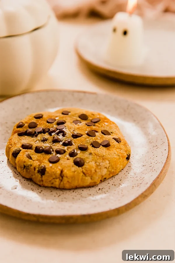A perfectly baked single-serve pumpkin cookie, golden brown and speckled with chocolate chips, resting on a rustic white plate.