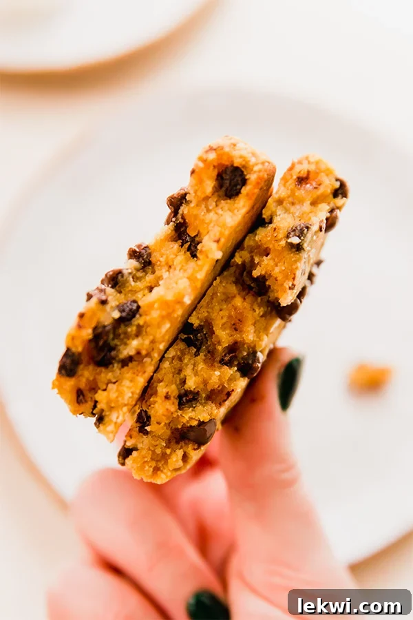 A single-serve pumpkin cookie gently split in half, revealing its moist, tender interior and abundant dairy-free chocolate chips, held in a hand.
