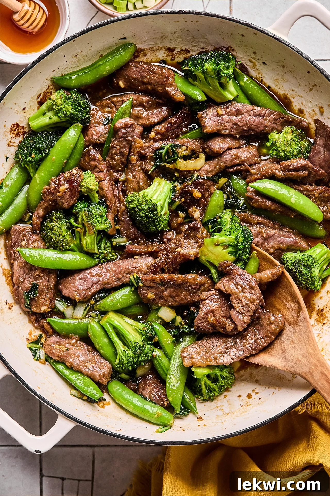 Honey garlic beef stir fry in a pan with a wooden spoon.