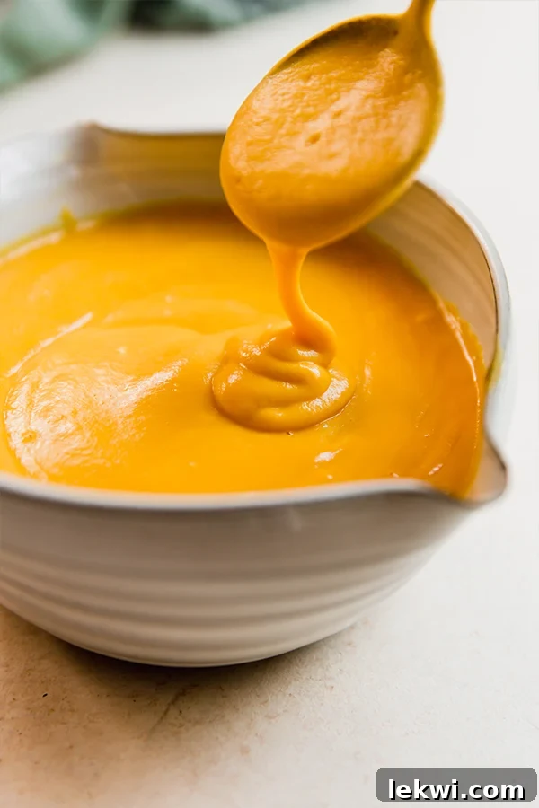 A spoon expertly drizzling thick, golden dairy-free cheese sauce over a dish, showcasing its creamy texture.