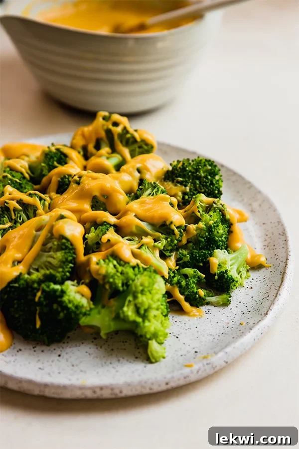 A plate of colorful roasted vegetables generously coated with a smooth, golden dairy-free cheese sauce, ready to be enjoyed.