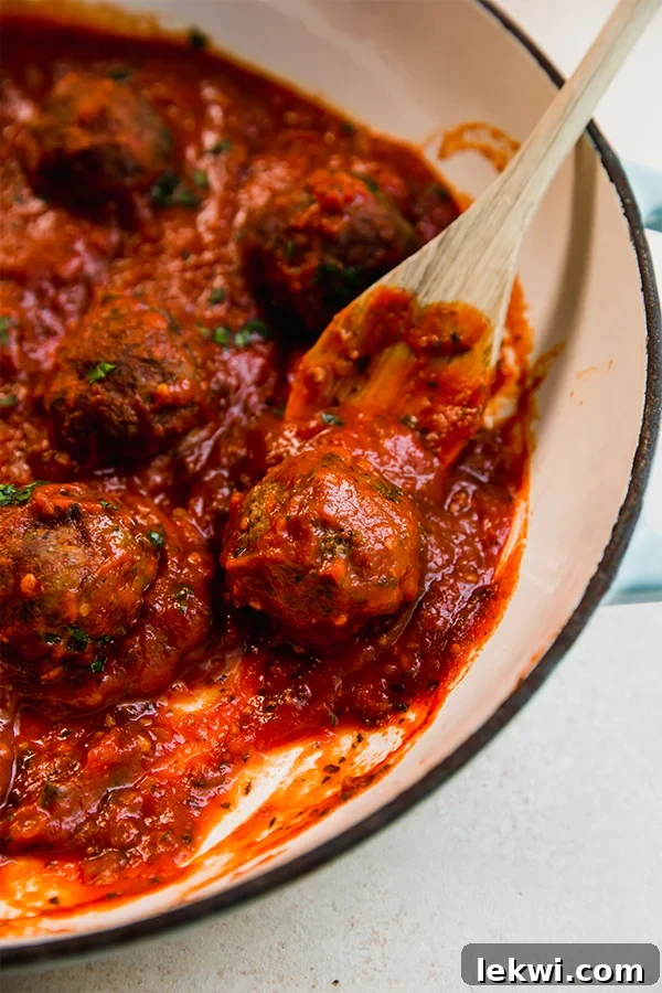 Wooden spoon scooping an Italian lamb meatball from a pan.