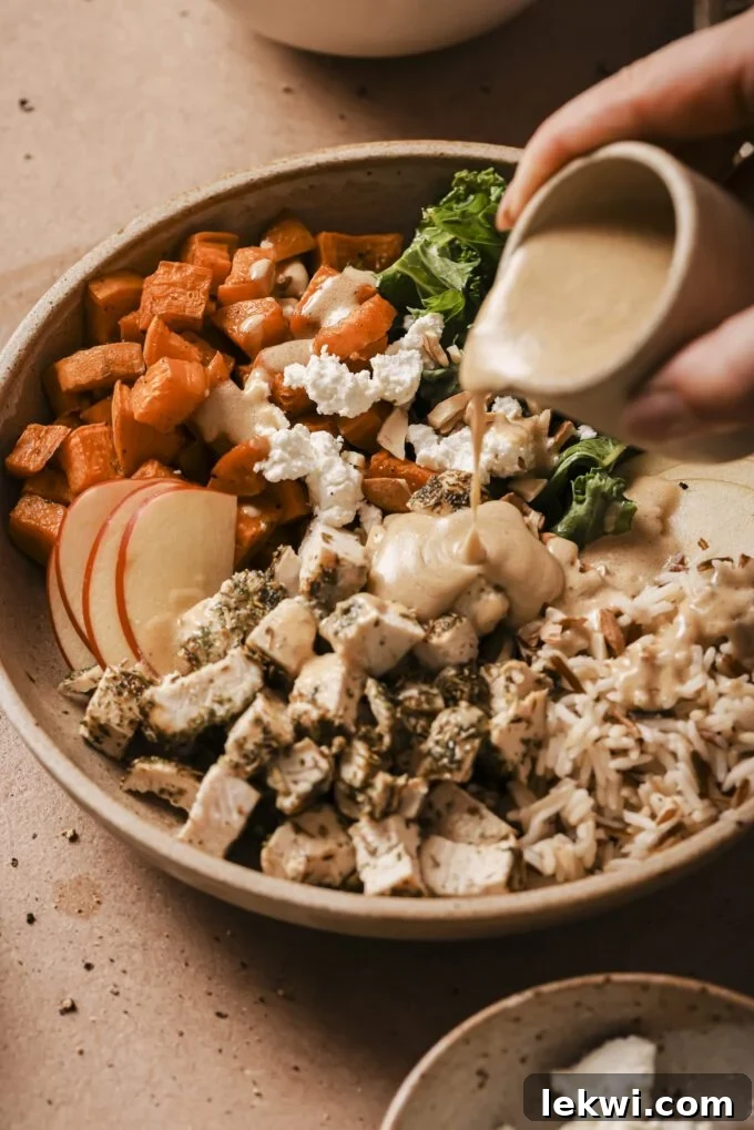 Harvest bowl with sweet potato, kale, chicken, rice, sweet potato and dressing being poured over.
