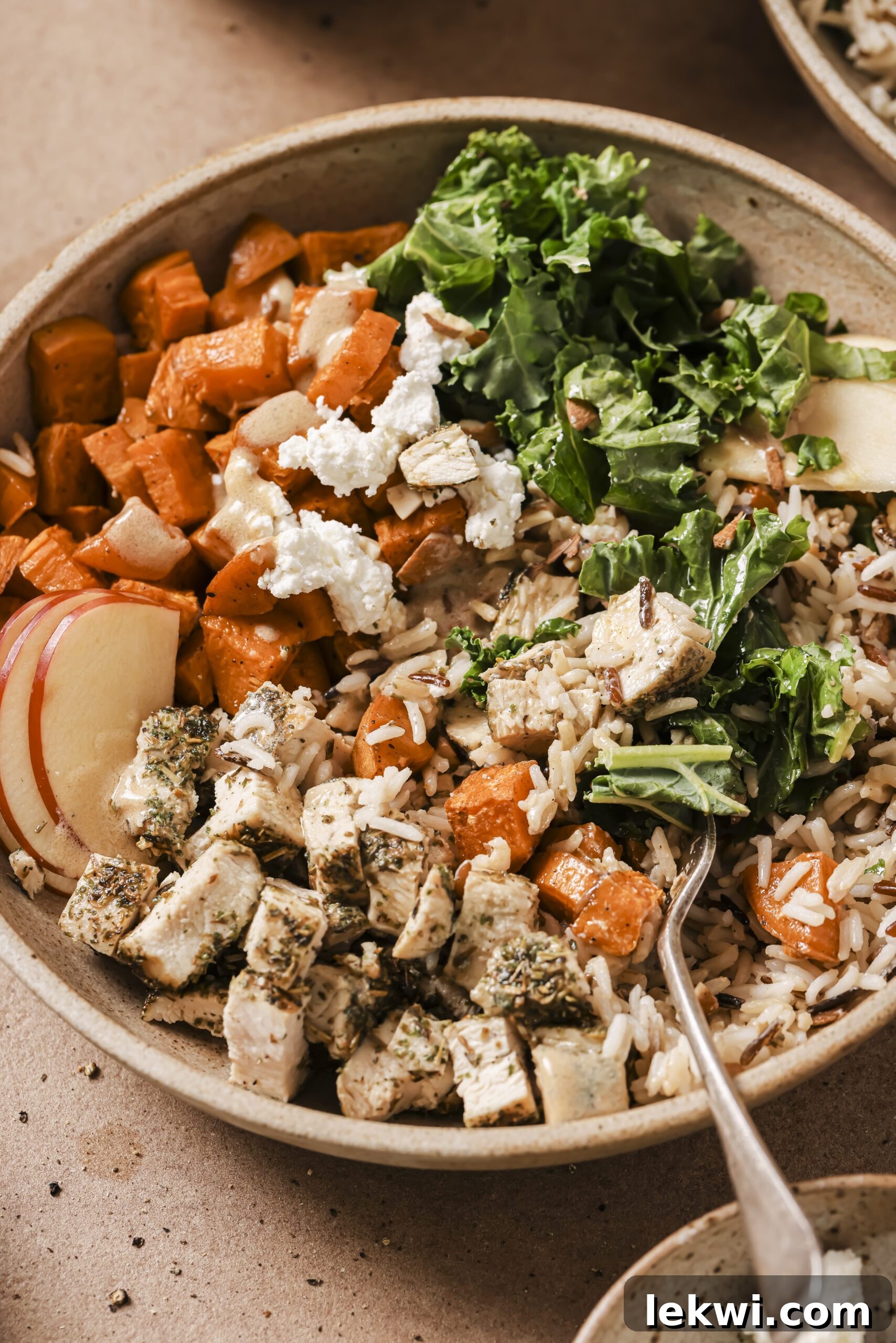 Harvest bowl with sweet potato, kale, chicken, rice, sweet potato and dressing in a bowl with a fork.