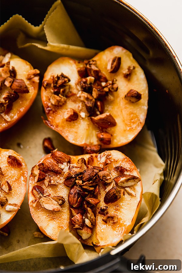 Cooked apple halves in an air fryer basket, showing soft, caramelized flesh and perfectly toasted almond toppings.