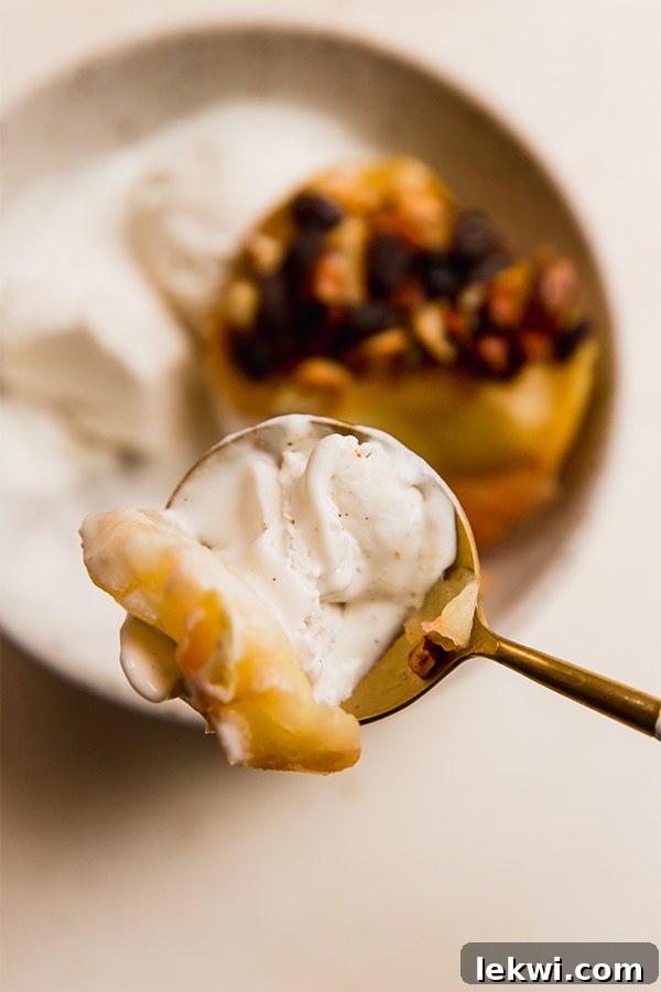 A close-up of a spoonful of warm air fryer baked apples and dairy-free ice cream, showing the soft texture and inviting steam.