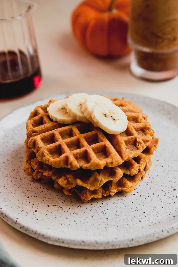 Pumpkin waffles stacked on a plate, drizzled with maple syrup and sliced banana.