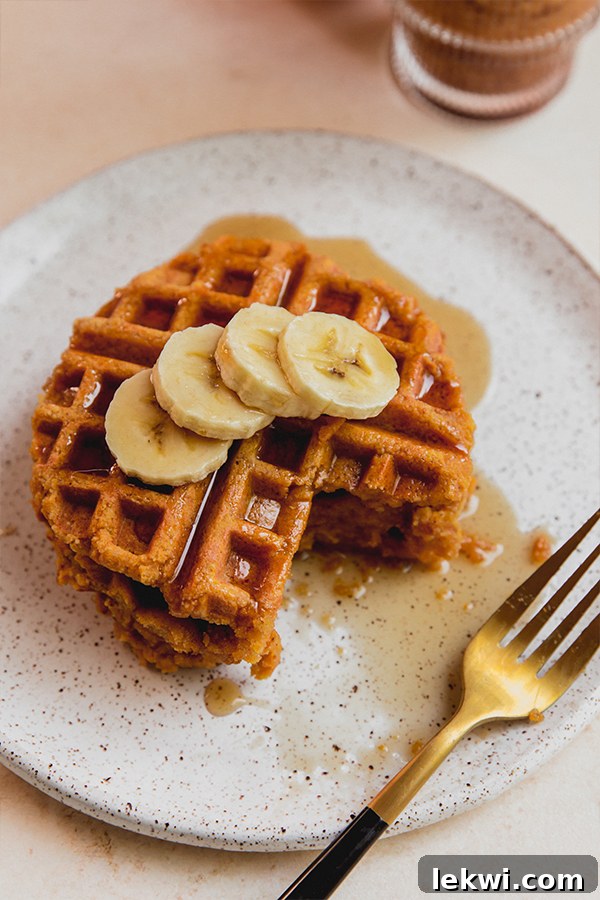 A stack of golden pumpkin waffles with sliced banana and a drizzle of maple syrup.