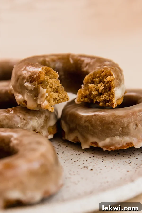 A stack of three apple cider donuts, with one having a bite taken out of it, showcasing the soft interior.