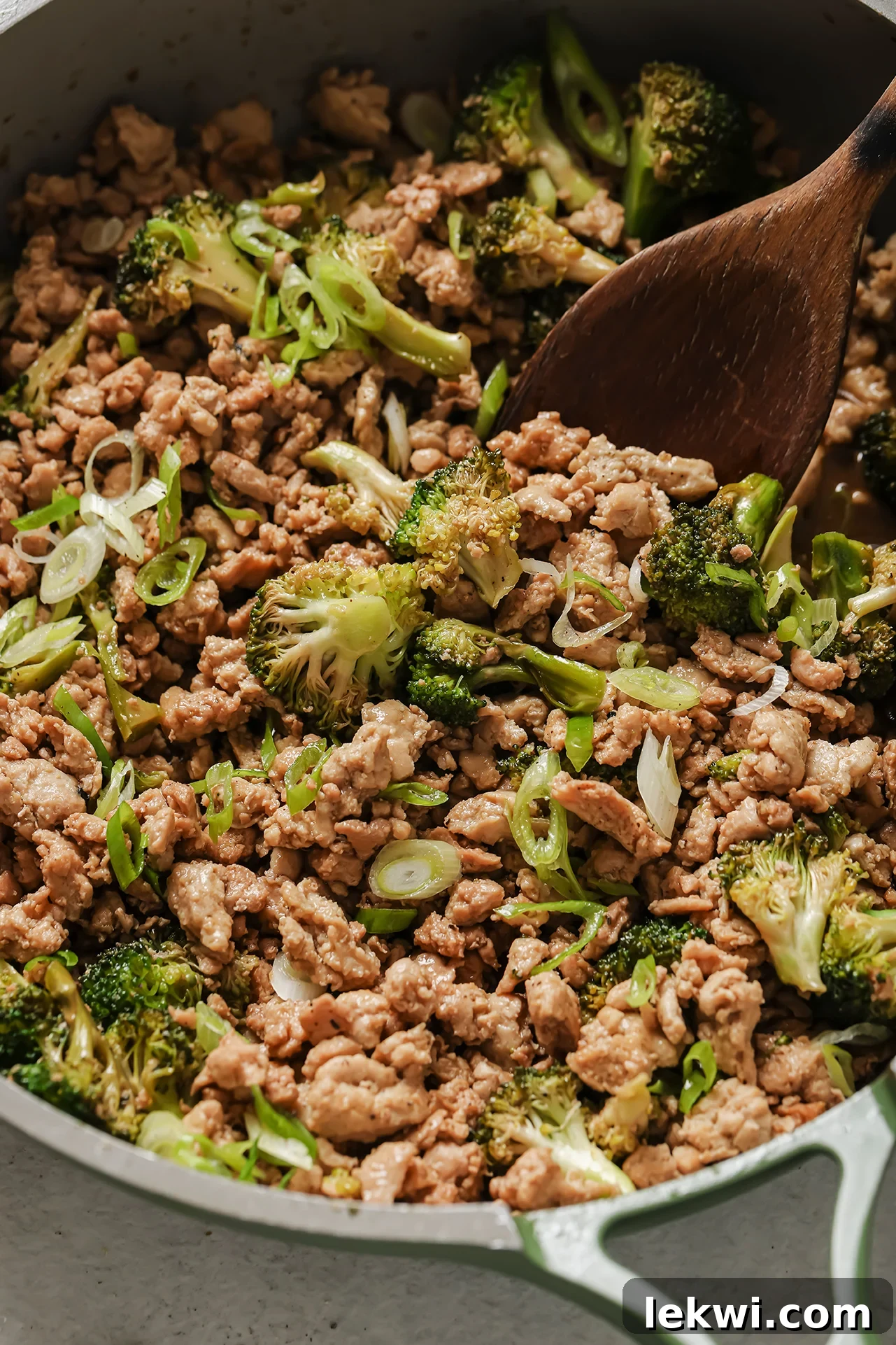 Ground chicken and broccoli in a green pan with a wooden spoon.