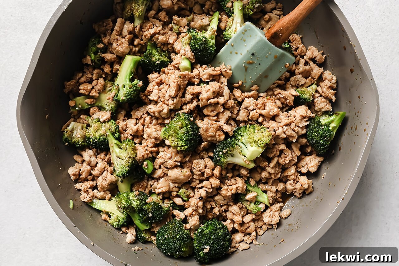 Ground chicken and broccoli fully cooked in a pan with a spatula.