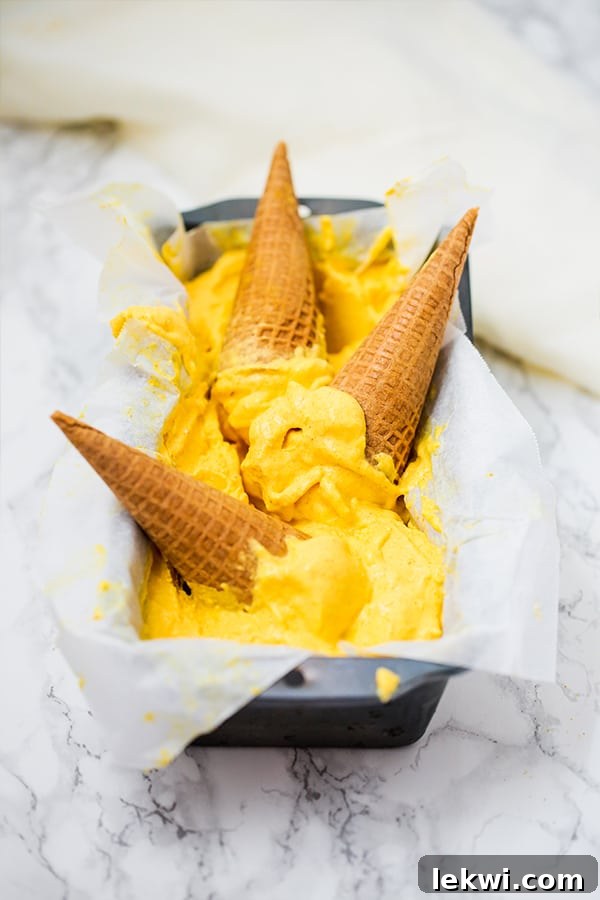 A loaf pan filled with vibrant mango turmeric ice cream and three ice cream cones resting on top.