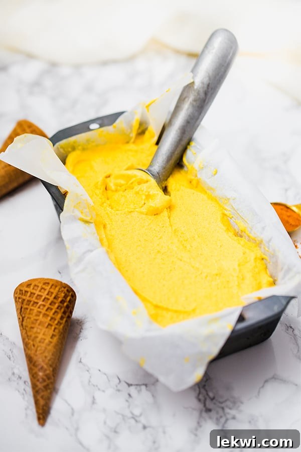 A loaf pan filled with mango turmeric ice cream and an ice cream scoop nestled within it.