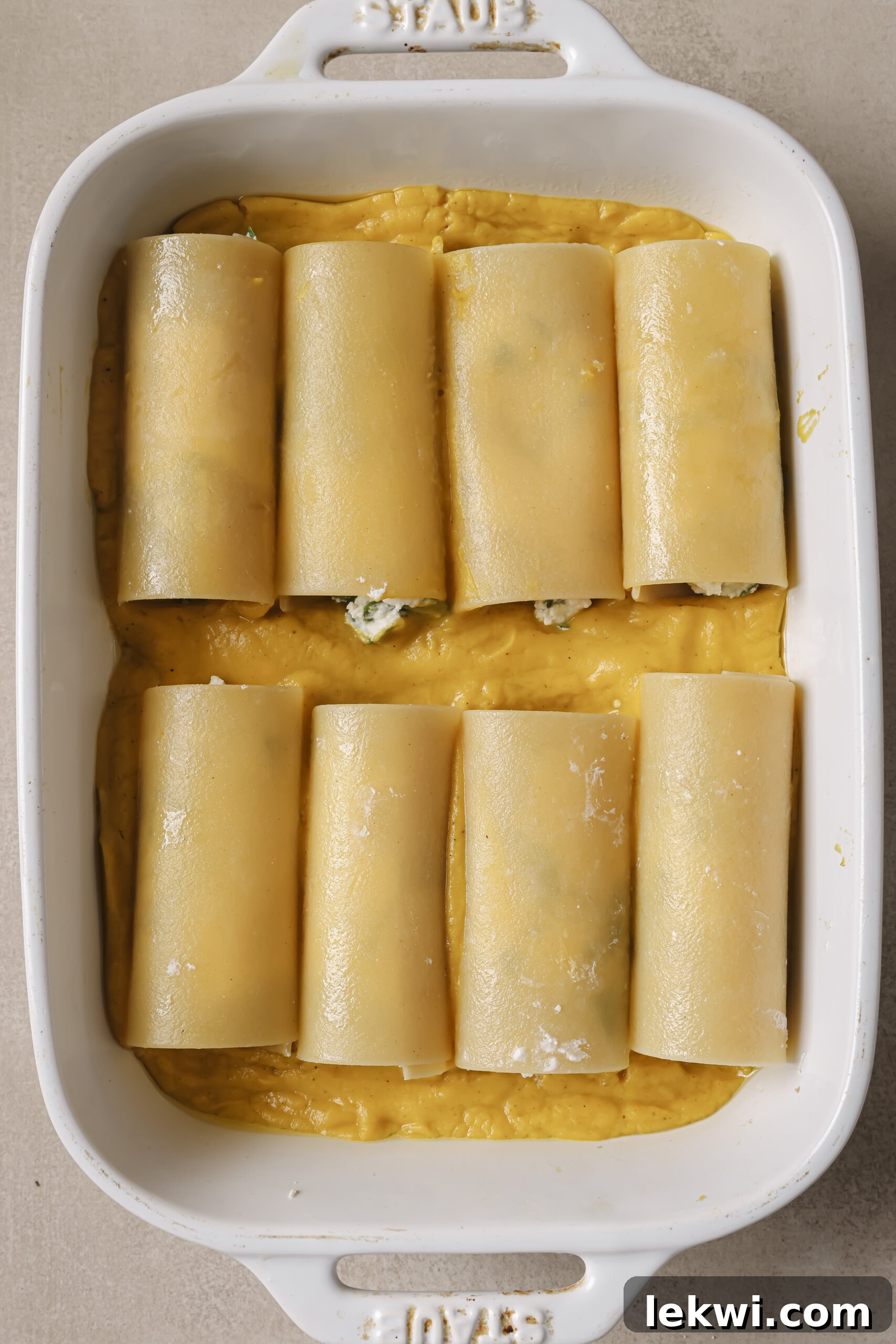 Lasagna roll ups laying in a baking dish on top of butternut squash sauce.