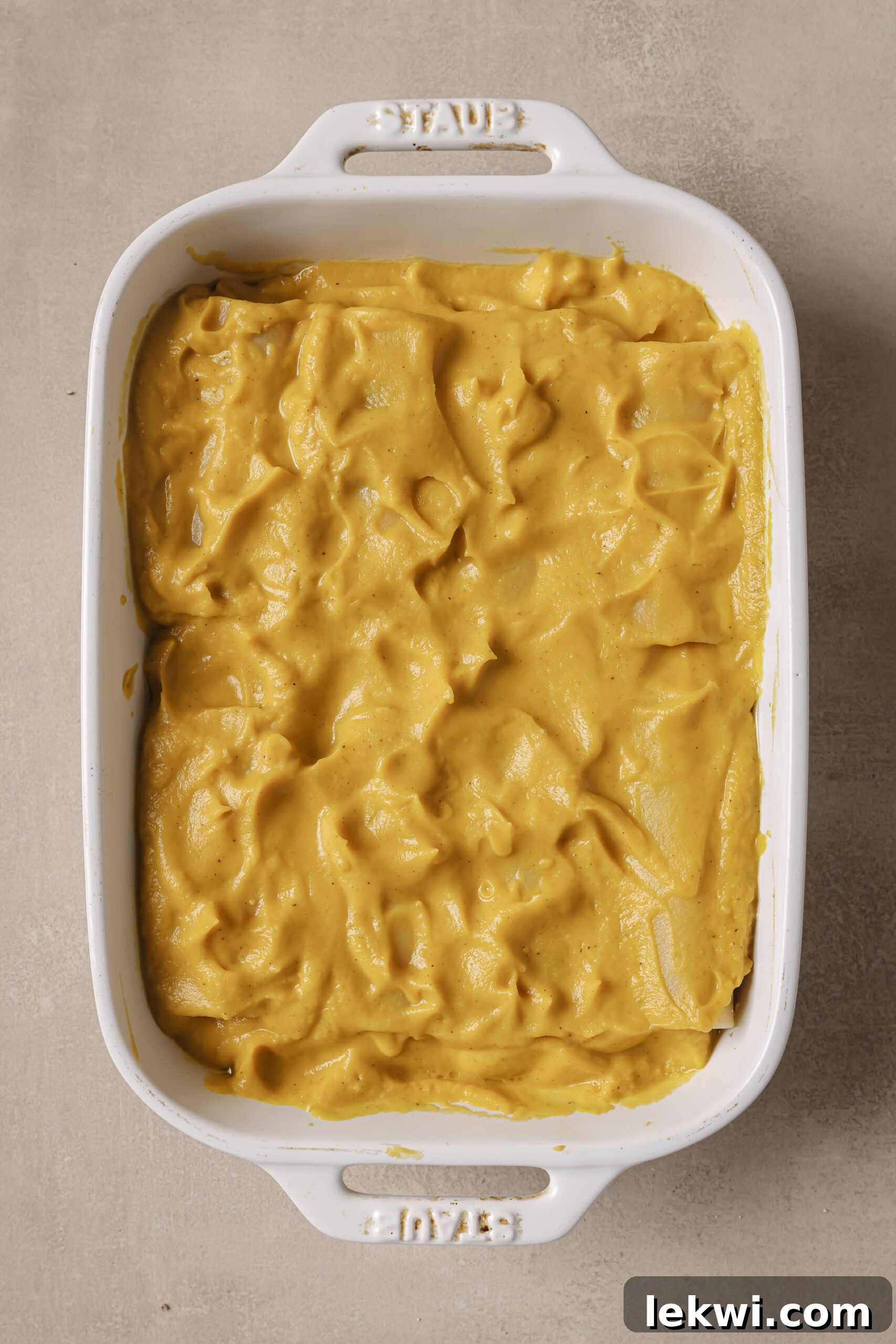 Lasagna roll ups laying in a baking dish on top of butternut squash sauce, with more sauce on top.