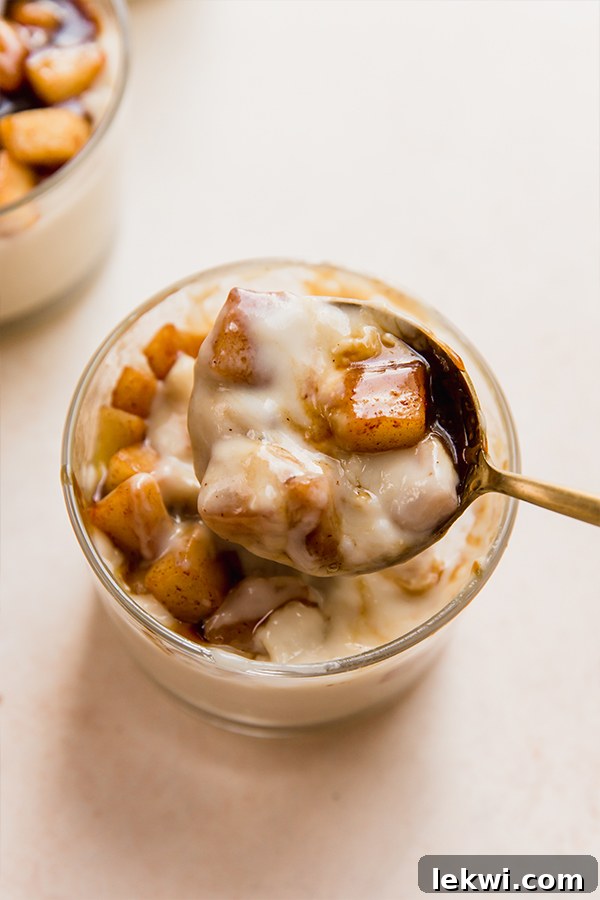 A single serving cup of dairy-free caramel vanilla pudding, beautifully topped with apples and caramel, with a spoon gently resting in it, ready to be enjoyed.