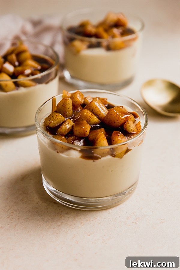 A close-up shot of a single cup of dairy-free caramel vanilla pudding, showcasing its creamy texture, topped with perfectly caramelized apples and a rich caramel drizzle, ready to be enjoyed.