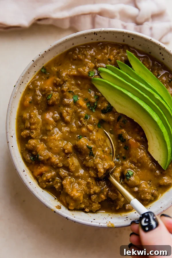 Spoon in a bowl of dairy-free queso chili topped with avocado slices and fresh cilantro.