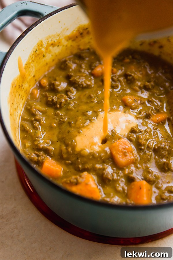 A large pot of dairy-free queso chili simmering on a stovetop, exuding warmth and rich aroma.