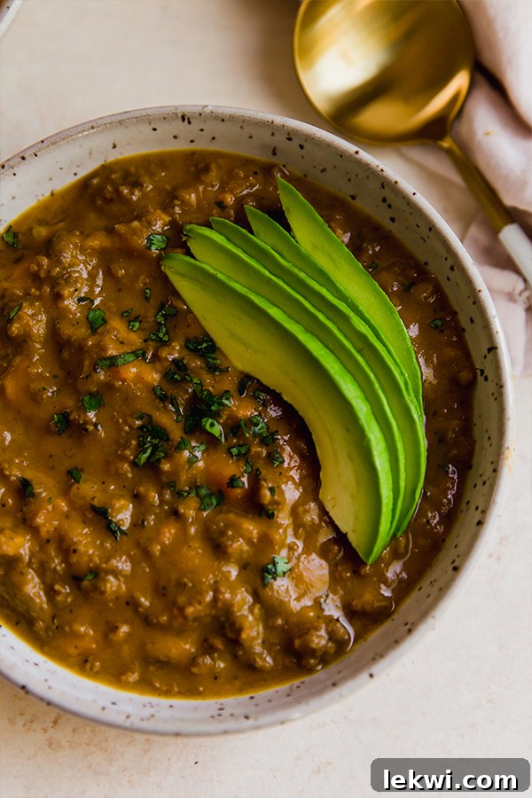 A bowl of dairy-free queso chili garnished with fresh avocado slices and herbs.