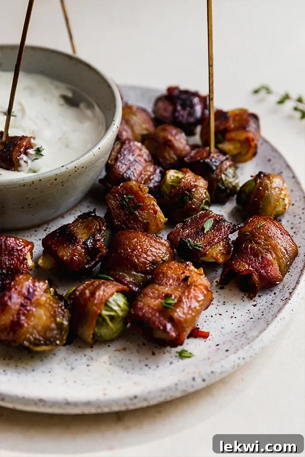 Bacon wrapped brussels sprouts on a plate with a bowl of dip.