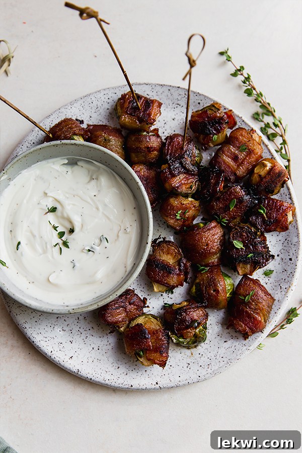A platter with bacon wrapped brussels sprouts and dipping sauce.
