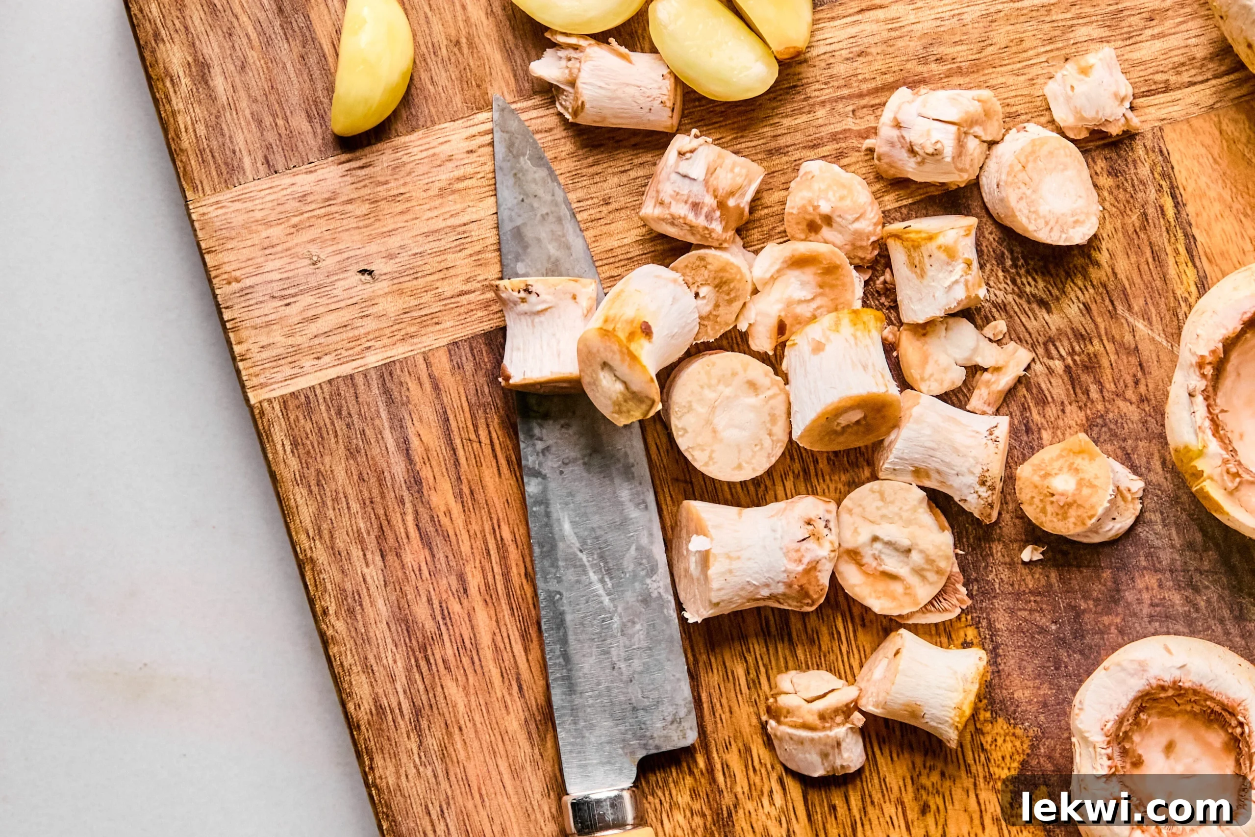 A cutting board with neatly sliced garlic and the removed stems of white button mushrooms, ready for preparation.