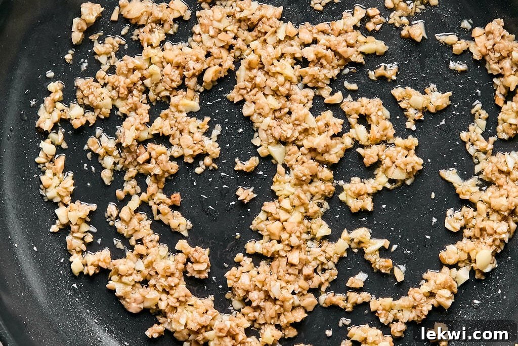 A pan with finely chopped garlic and mushroom stems lightly sizzling in avocado oil, releasing a fragrant aroma.