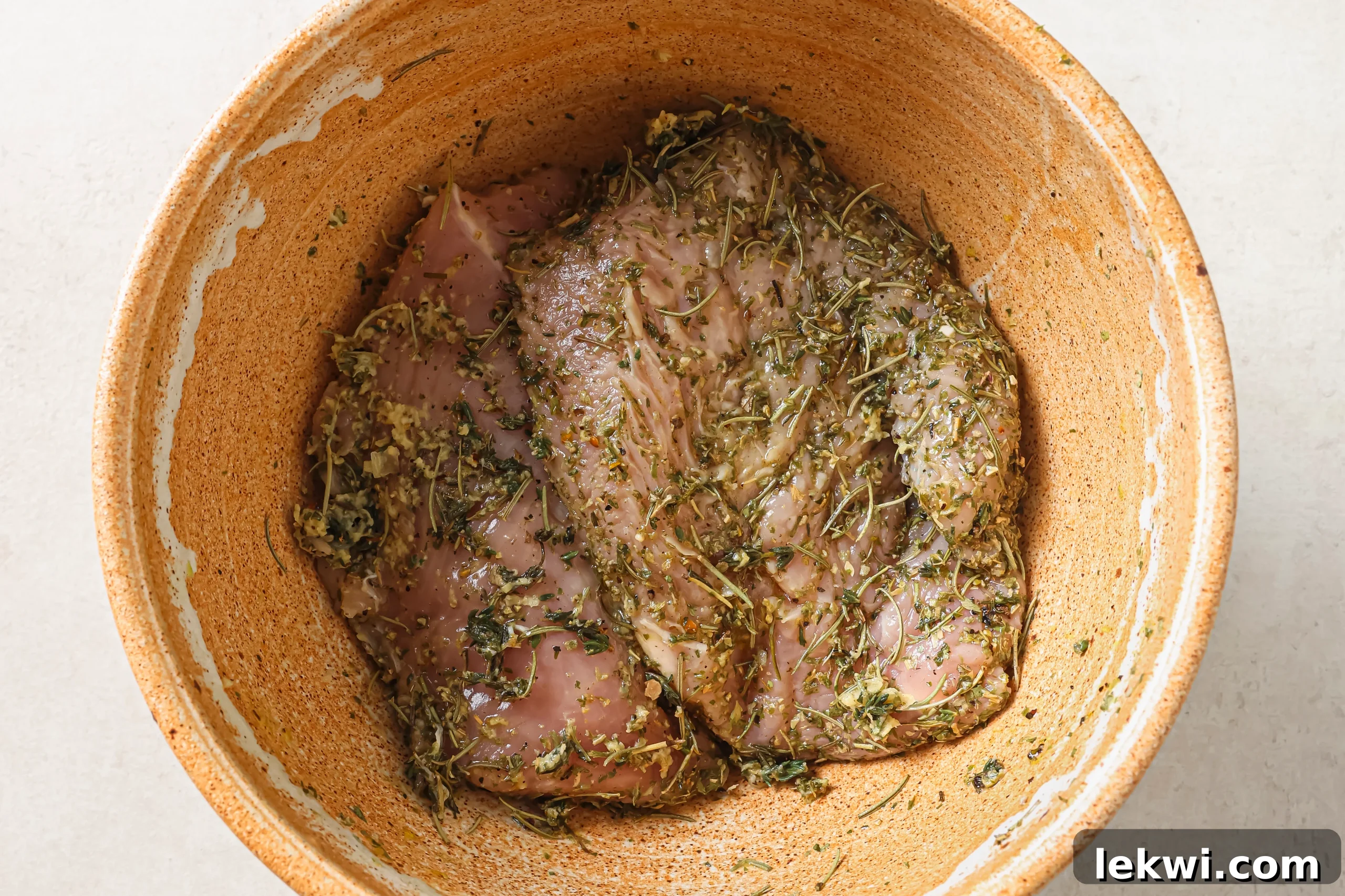 Turkey tenderloin marinating in a bowl, coated in a rich, herb-infused mixture.