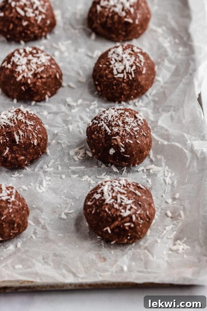 A rustic baking sheet neatly arranged with a collection of dark chocolate collagen protein bites, each adorned with a generous sprinkle of shredded coconut, perfectly set and ready to be served.