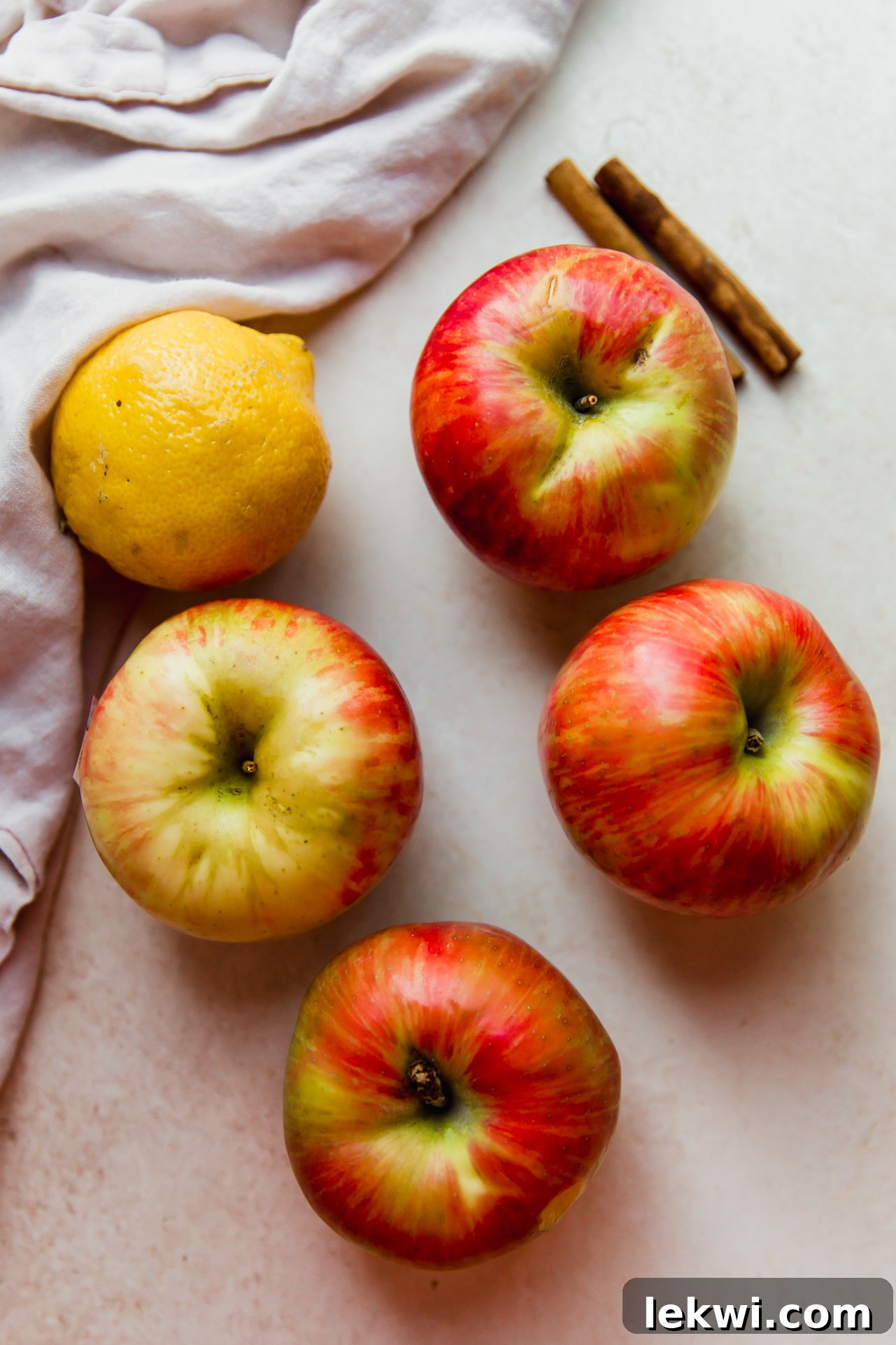Collection of fresh apples, coconut sugar, lemon, apple cider, and cinnamon sticks – ingredients for homemade applesauce.
