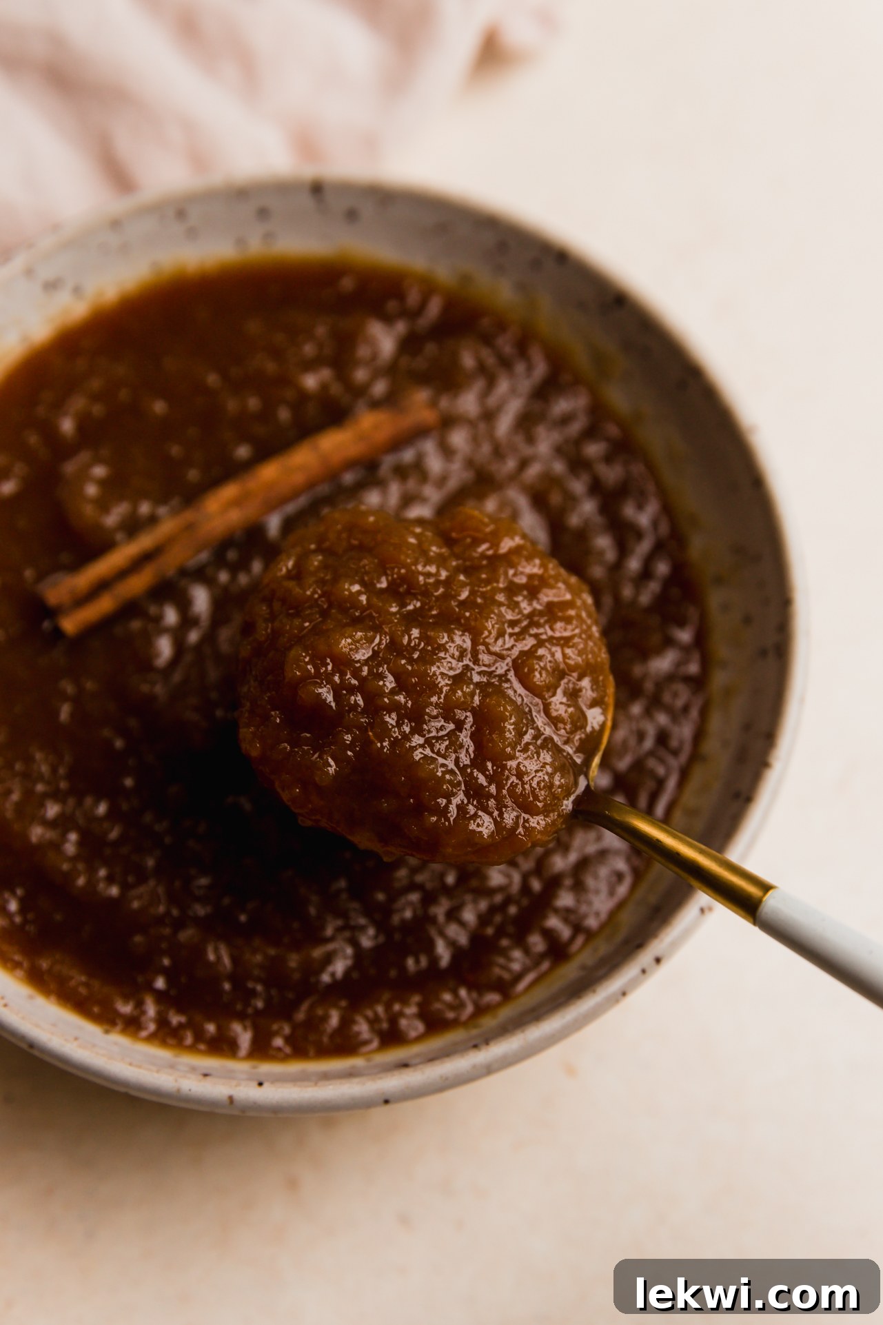 A spoon scooping creamy, homemade slow cooker applesauce from a bowl.