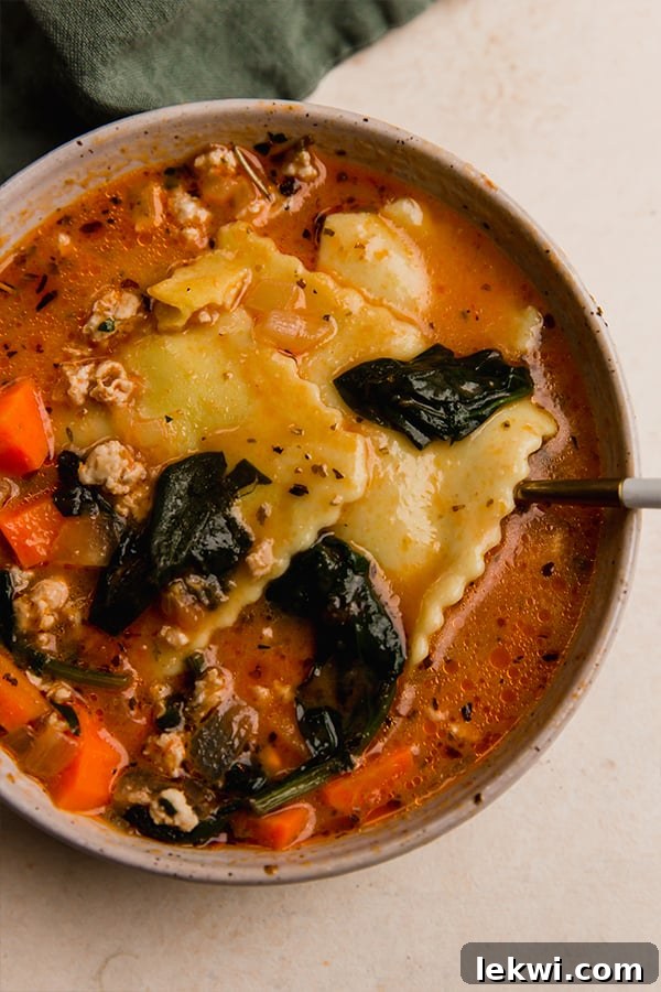 Bowl of creamy sausage ravioli soup with a spoon, garnished with fresh parsley.