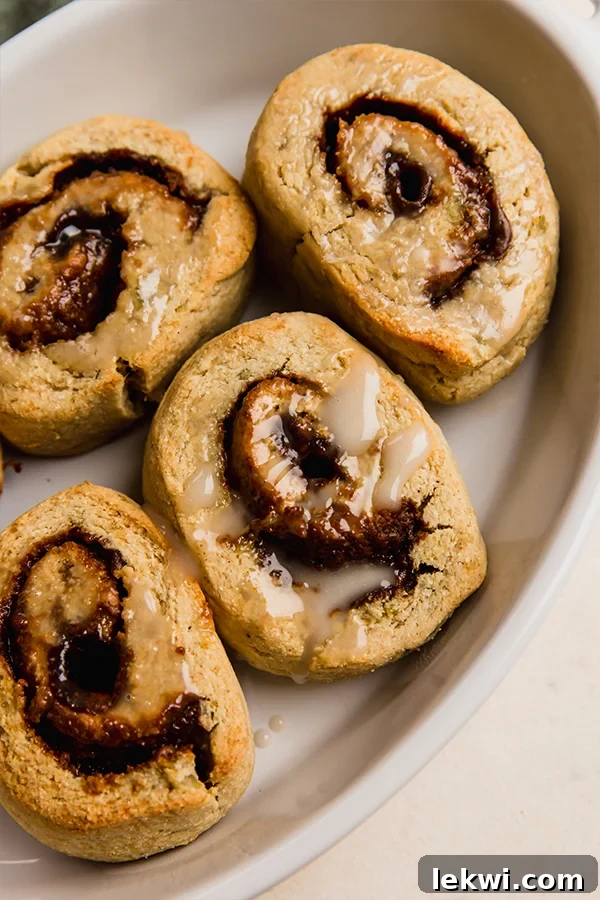 AIP gingerbread cinnamon rolls topped with coconut butter icing, nestled in a baking dish, ready to be enjoyed.