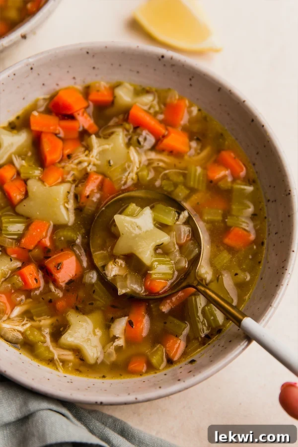 Spoon scooping gluten-free chicken and stars soup from a bowl, highlighting the star-shaped 'pasta' and tender chicken.