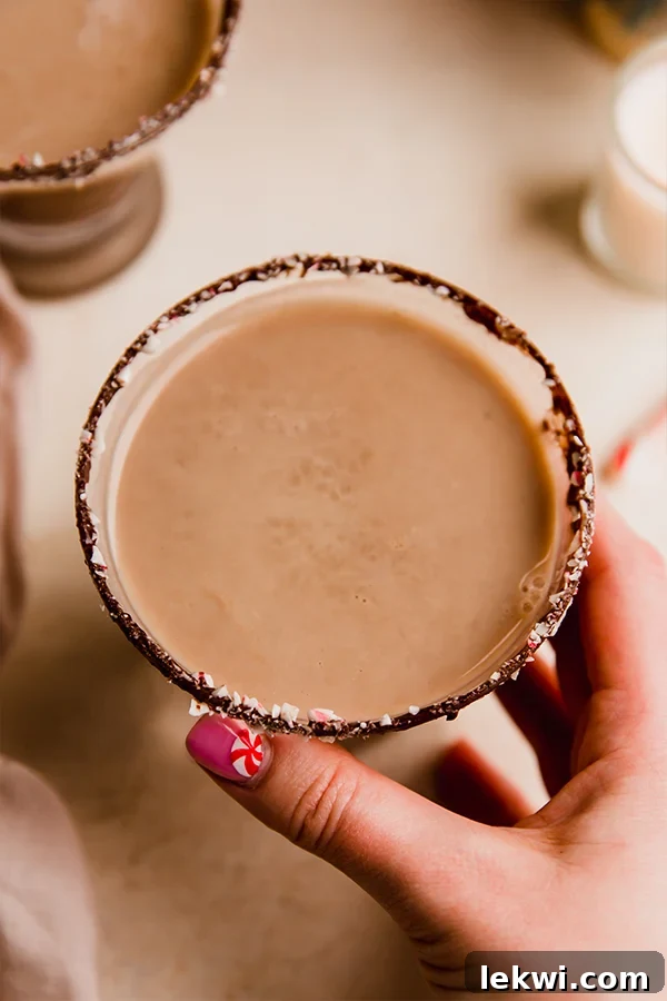 Person grabbing a glass of peppermint mocktail with a chocolate rim.