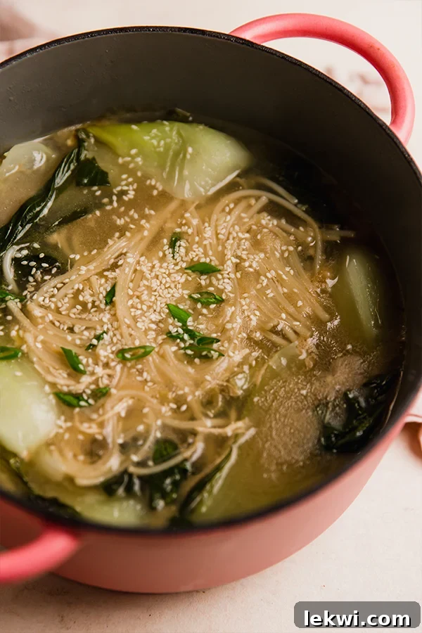 A pot of Bok Choy Noodle Soup simmering on the stove, showing the noodles and bok choy cooking in the broth.