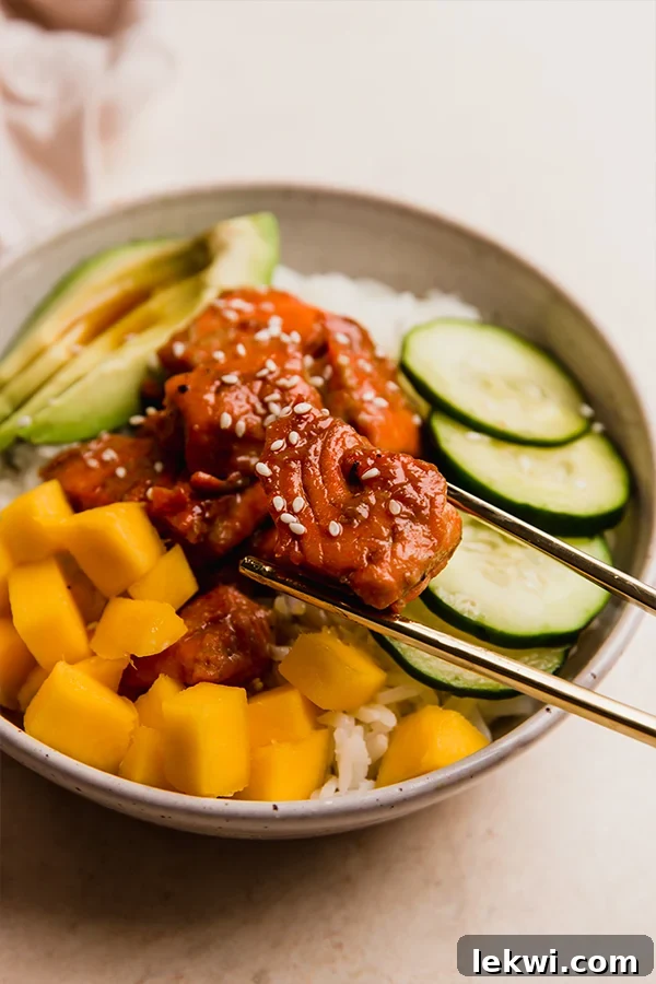Chopsticks grabbing a piece of garlic ginger salmon from a bowl.