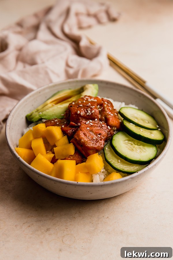 Mango, cucumbers, avocado, and garlic ginger salmon in a bowl over rice.