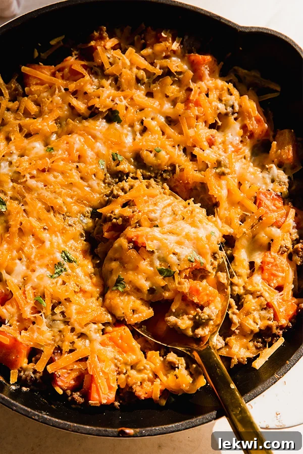 A dairy-free cheesy beef & sweet potato skillet with a serving spoon.