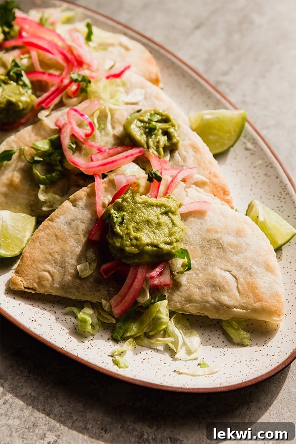 A beautifully arranged platter of baked shredded beef tacos, topped with vibrant pickled red onions, creamy guacamole, and fresh cilantro, ready for serving.