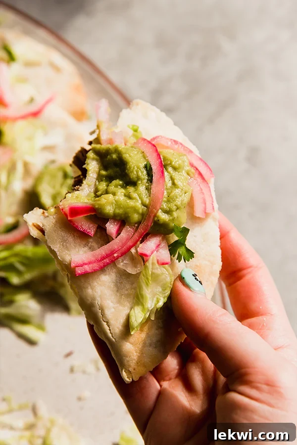 A single crispy baked shredded beef taco held in a hand, showcasing its perfect golden-brown texture and appealing filling.