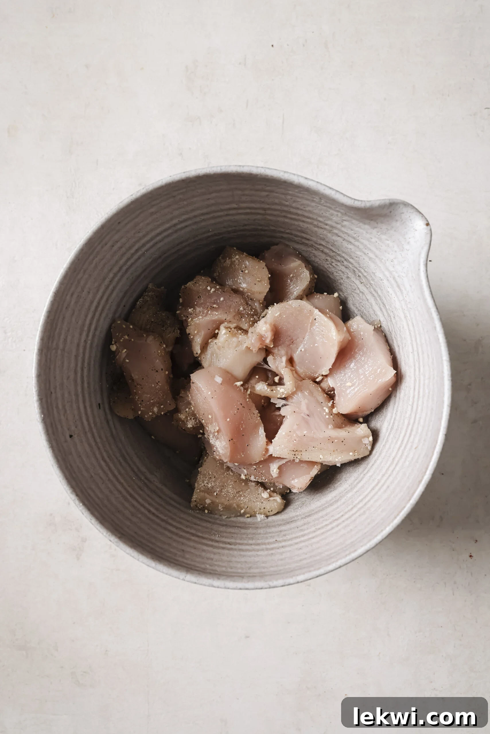 Raw cubed chicken tossed with seasonings in a bowl.