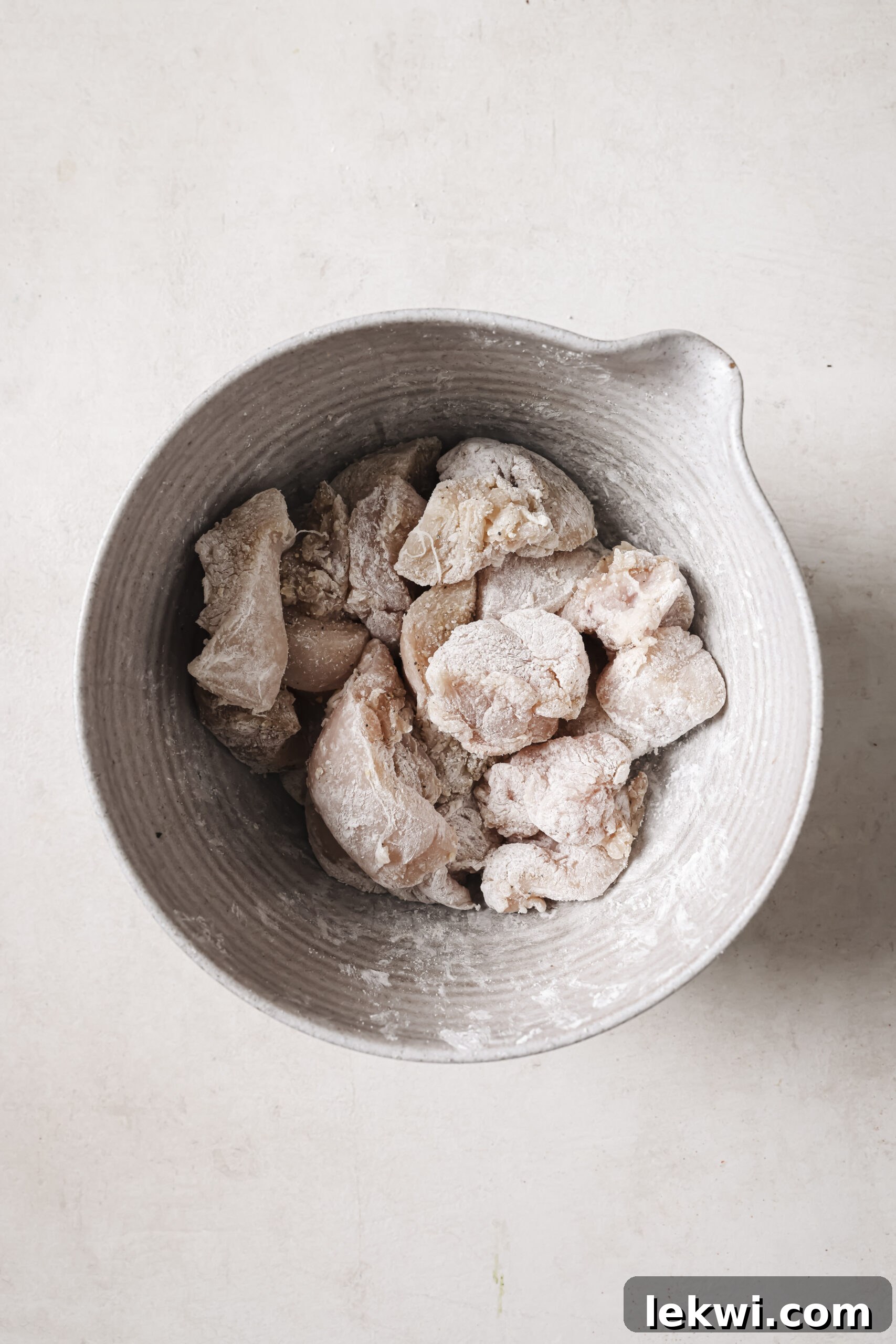 Raw cubed chicken tossed with arrowroot starch in a bowl.