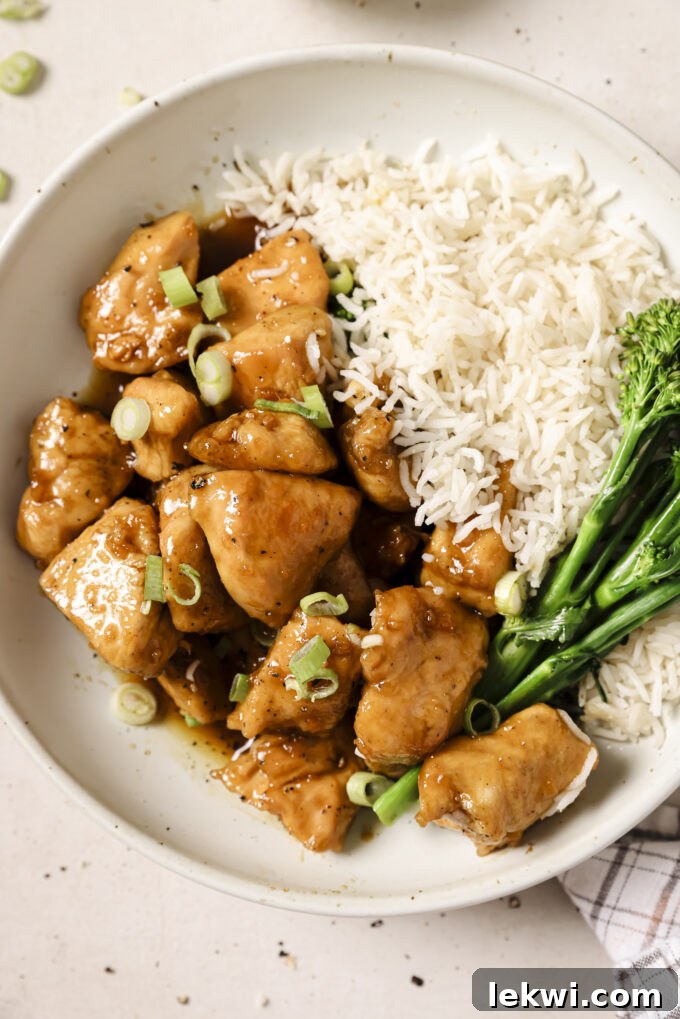 Honey butter chicken bites in a bowl topped with green onion and served with rice and broccoli.