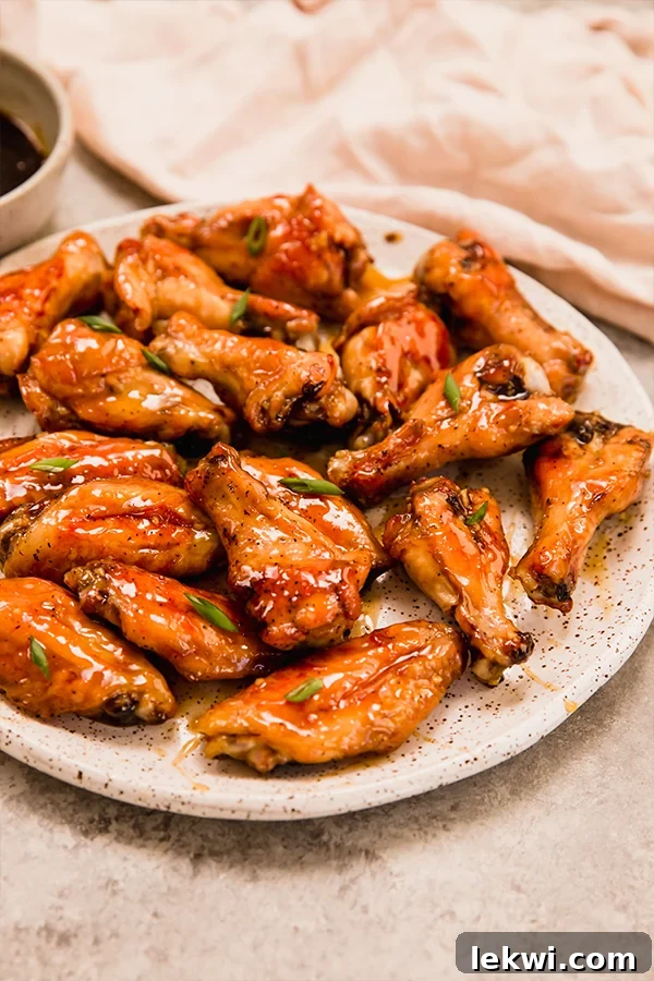 A close-up shot of a plate filled with golden-brown baked honey-garlic chicken wings, garnished with chopped green onions.