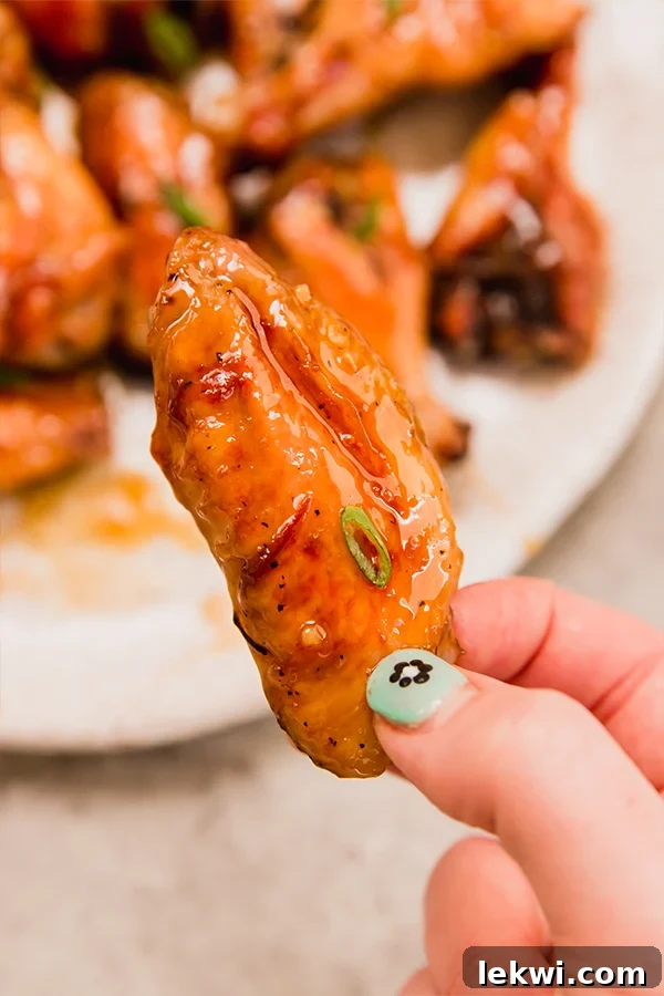 A close-up of a hand holding a honey garlic chicken wing, showcasing its sticky glaze and crispy texture.